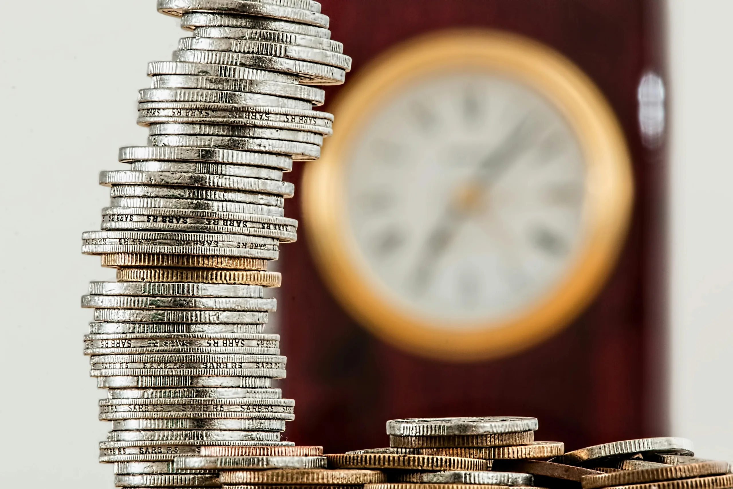 a stack of silver coins with an out of focus clock in the backgrounds. Accompanies blog on state pension.