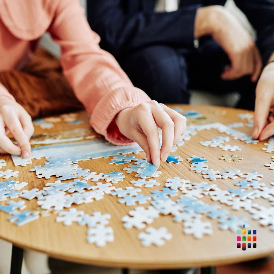 two people putting together a jigsaw puzzle on a table. only their hands are visible.