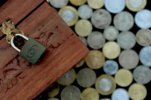 decorative image of a wooden box with a padlock on top and coins on the table underneath