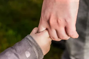 decorative image of an adult hand and a child's hand holding their finger. to accompany an article on trusts and trusee responsibilities in financial planning and getting your financial house in order