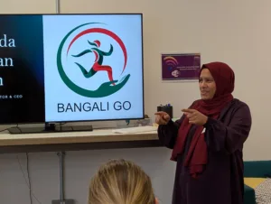 Majeda from Bangali Go stands in front of a TV screen showing a presentation. Social Ventures Pitch Event