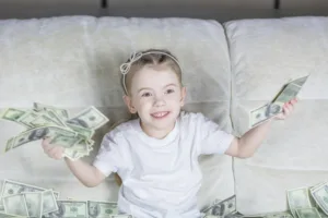 decorative image to accompany blog post on gifting and IHT. a young girl sits on a sofa surrounded by money notes while holding some in both her hands. she has a big grin on her face.