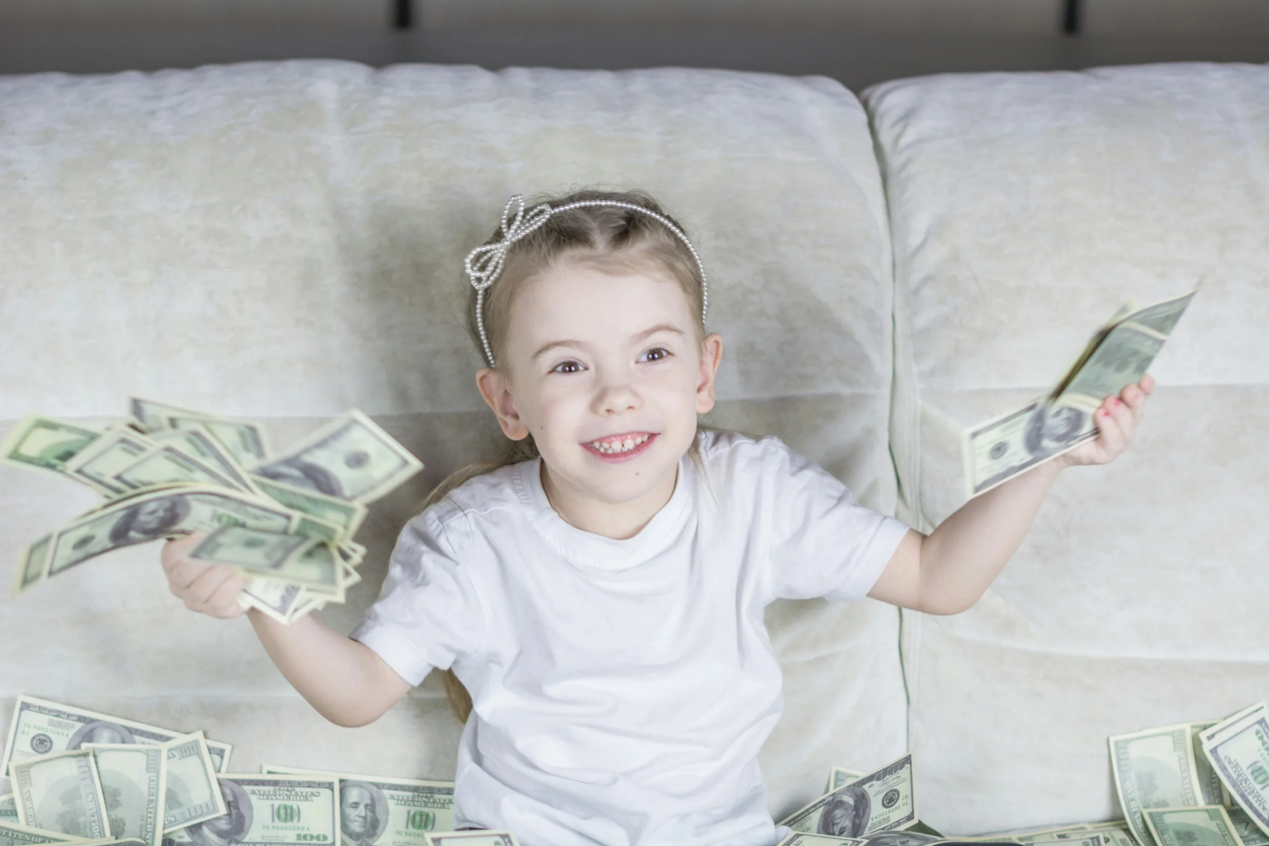 decorative image to accompany blog post on gifting and IHT. a young girl sits on a sofa surrounded by money notes while holding some in both her hands. she has a big grin on her face.